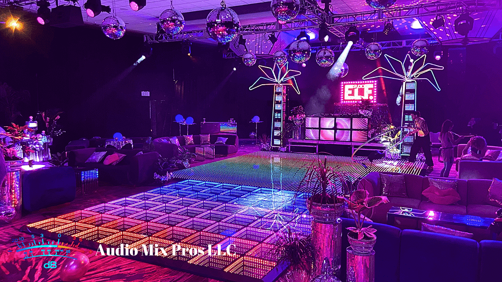 A vibrant event space featuring a lit dance floor with colorful lights, disco balls hanging from the ceiling, a DJ booth, and lounge seating adorned with plants and decorative elements.